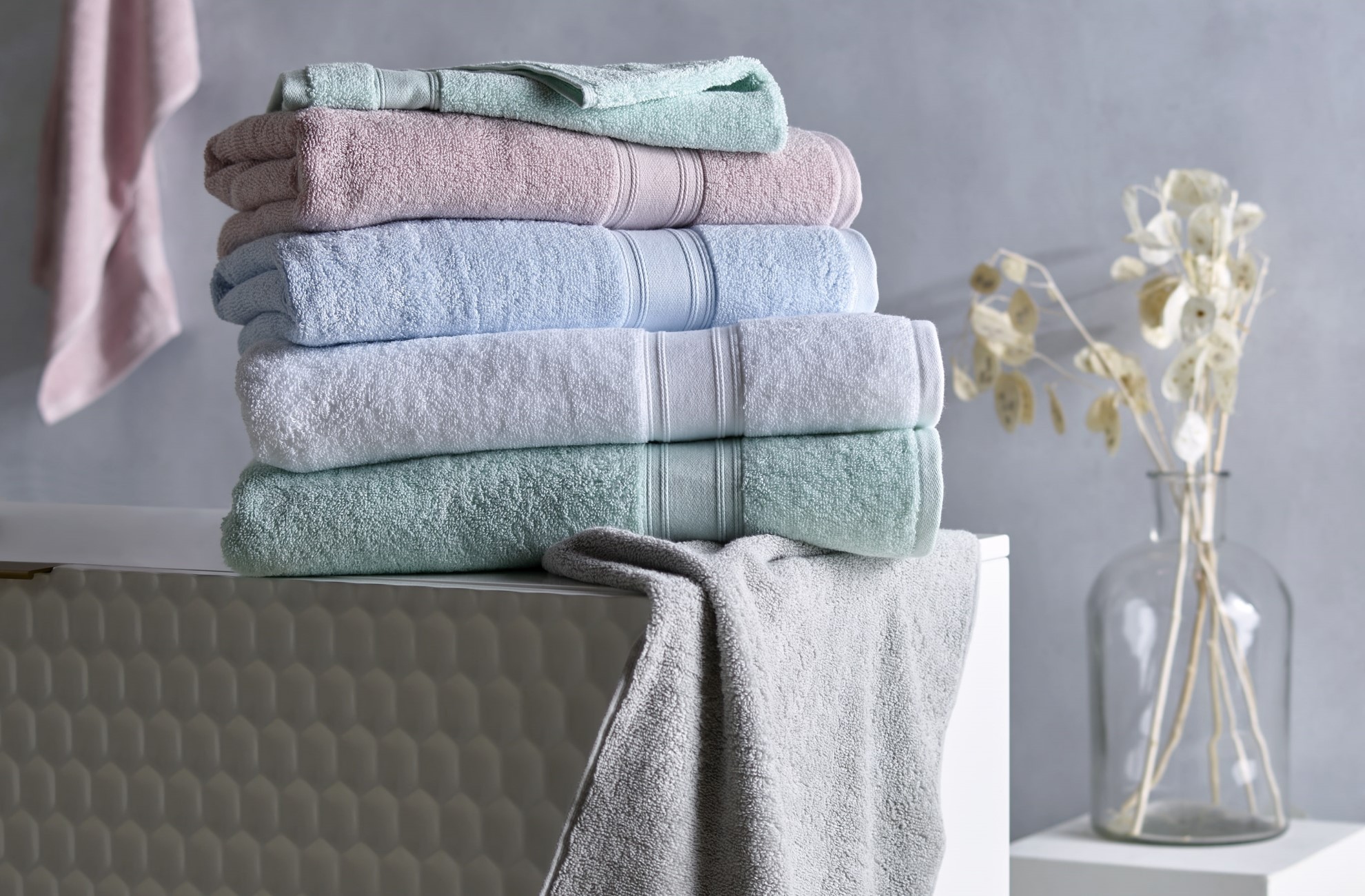 Pastel coloured KOO Bath Towels folded and stacked in a bathroom